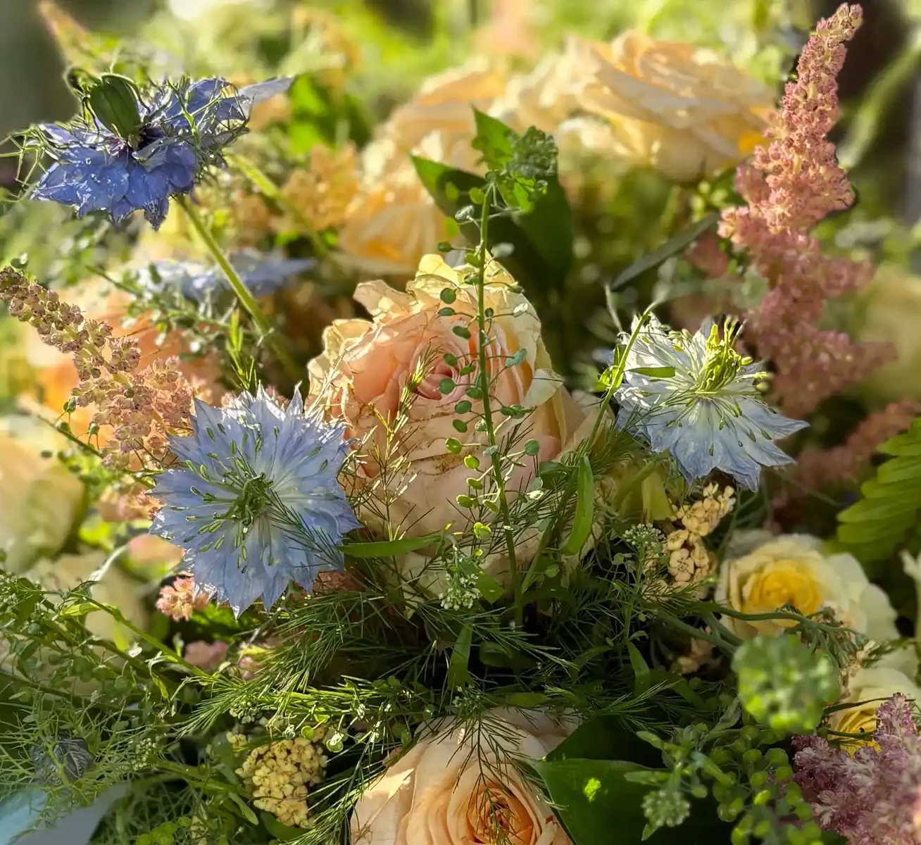 pink, peach, and blue blooms amongst green foliage forming a bouquet